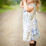 girl with blonde hair and wearing blue and white plaid dress and capturing picture during daytime